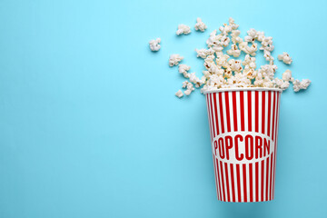 Overturned paper cup with delicious popcorn on light blue background, flat lay. Space for text