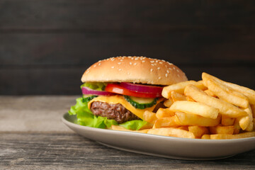 Delicious burger and french fries served on wooden table, closeup. Space for text