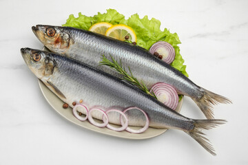 Plate with salted herrings, onion rings, slices of lemon, peppercorns and lettuce on white marble...