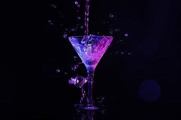 Pouring martini. Glass and splashes in neon lights on dark background, bokeh effect