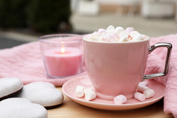 Cup of tasty cocoa with marshmallows, pink sweater, cookies and burning candle on wooden table outdoors