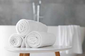 Rolled white towels on stool in bathroom. Space for text
