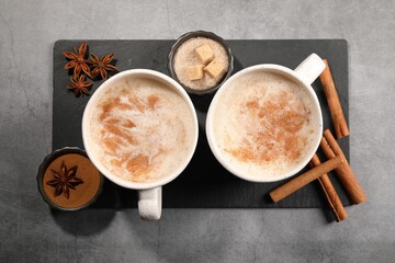 Cups of delicious eggnog with anise and cinnamon on grey table, flat lay