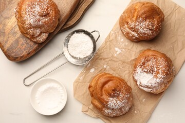 Delicious profiteroles with powdered sugar on white table, flat lay