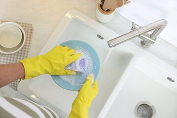 Man washing plate in kitchen sink, top view