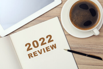Text 2022 Review written in notebook, pen, tablet and cup of coffee on wooden table