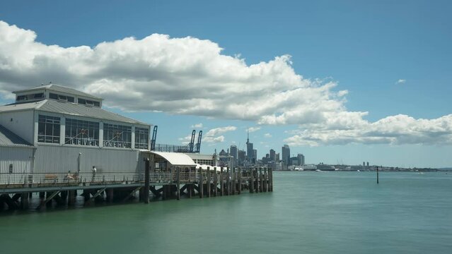 Time lapse of Devonport Wharf with Auckland City centre viewed across the Waitematā Harbour in the background. White, puffy, cumulus clouds forming over the city. boats moving to and fro. 