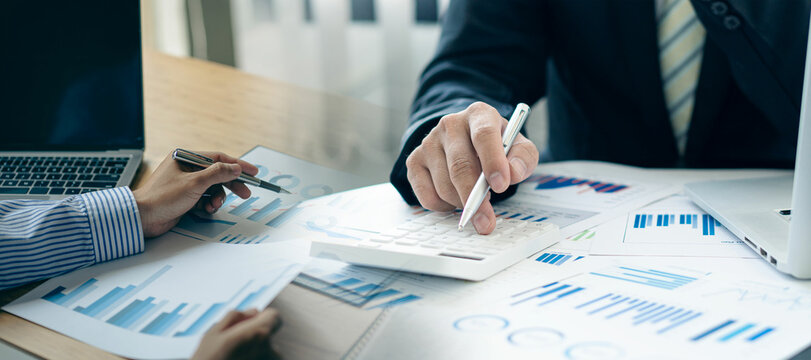 Business colleague working and analyzing financial figures on paper documents, accounts, contracts, investment consultant, corporate marketing plans using laptop and analytical technology.