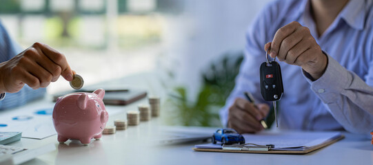 Hand holding coins in piggy bank and car salesman holding car keys, concept of saving money in car title and paying taxes