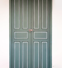 locking green wooden vintage door in Thailand with cement white creamy colour wall beside it.