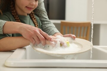 Mother and daughter washing plate above sink indoors, closeup
