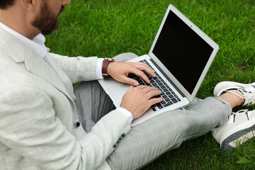 Businessman with laptop on green grass outdoors, closeup