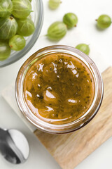 Jar of delicious gooseberry jam and fresh berries on white table, flat lay