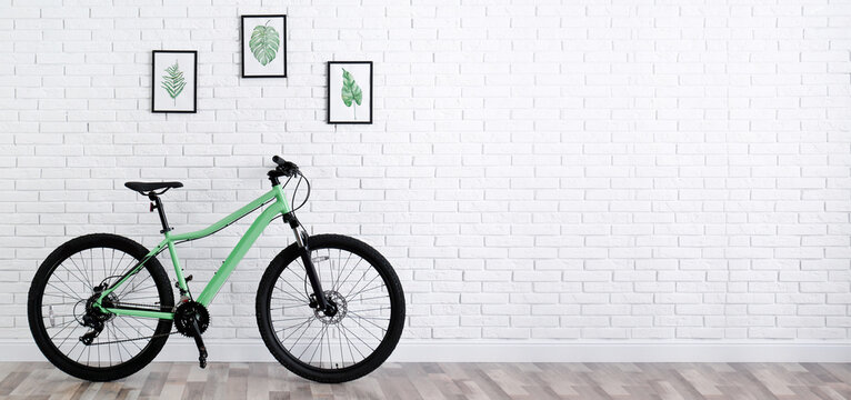 Modern green bicycle near white brick wall indoors, space for text. Banner design