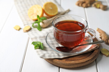 Cup of delicious ginger tea and ingredients on white wooden table, space for text