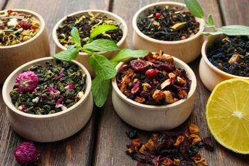 Different kinds of dry herbal tea in bowls on wooden table