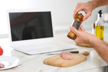 Man making dinner while watching online cooking course via laptop at table, closeup