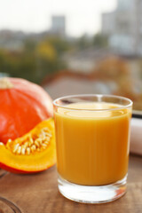 Glass with tasty pumpkin juice on wooden board indoors, closeup