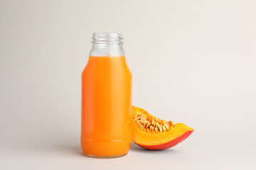 Tasty pumpkin juice in glass bottle and cut pumpkin on light background