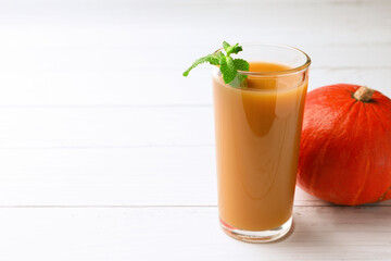 Tasty pumpkin juice in glass and whole pumpkin on white wooden table. Space for text