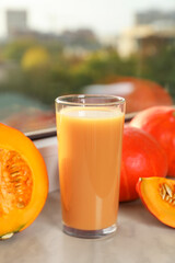 Tasty pumpkin juice in glass, whole and cut pumpkins on windowsill indoors