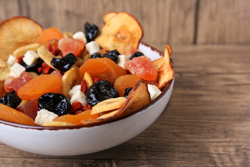 Bowl with different tasty dried fruits on wooden table, closeup. Space for text