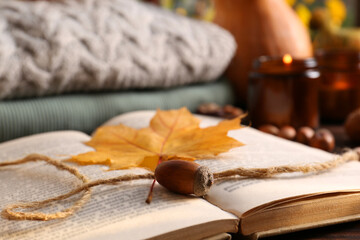 Naklejka na ściany i meble Book with autumn leaf as bookmark, acorn, scented candles and warm sweaters on wooden table, closeup