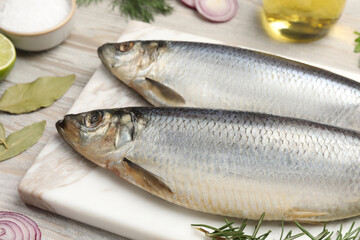 Delicious salted herrings and different ingredients on light wooden table, closeup