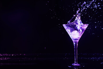 Glass of martini with ice and splashes in neon lights on dark background. Space for text