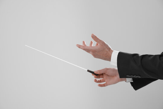 Professional conductor with baton on light grey background, closeup. Space for text