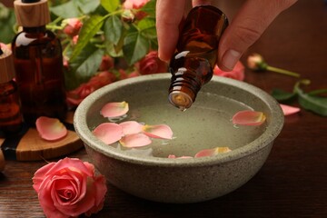 Woman dripping essential oil into bowl at wooden table, closeup. Aromatherapy treatment