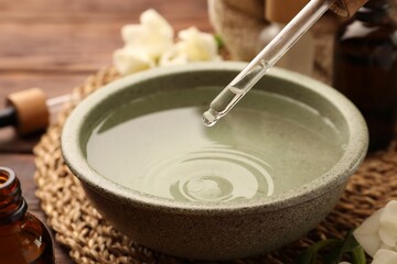 Dripping essential oil into bowl on wooden table, closeup. Aromatherapy treatment