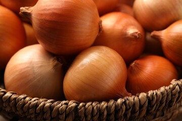 Wicker basket with many ripe onions on table, closeup