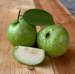 Closeup of a cut guava against a background of some guavas and green leaves and a wooden mat