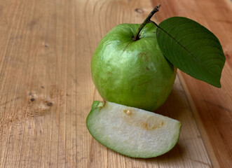 Closeup of a cut guava against a background of some guavas and green leaves and a wooden mat
