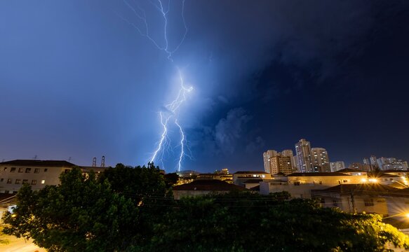 Lightning in the blue sky of the city. Summer storm. Thunder, lightning and rain at night. Santos, Brazil. 