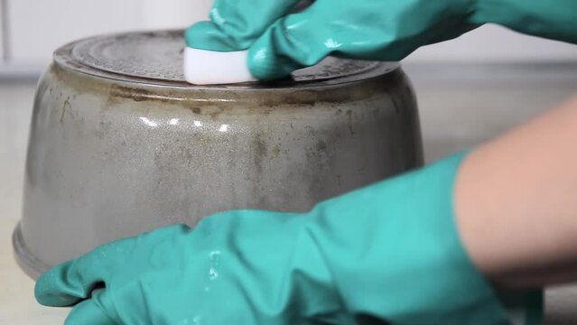 Hands in gloves cleaning old pot with eco friendly magic sponge, no detergent house cleaning. Cleaning in the home kitchen. Effective cleanser.Difficult to perform the task.