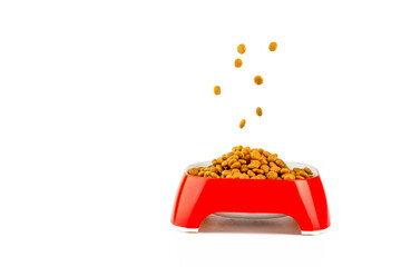 Pieces of dry food for cats and dogs fall into a red bowl on a white background.