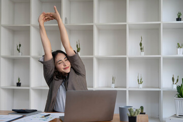 Asian businesswoman stretches her arms to relax her tired muscles from working at her desk all day at the office.