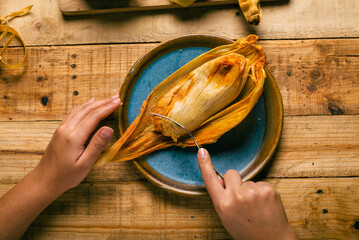 Hands of a person cutting a tamale with a fork. Tamale, typical Mexican food.