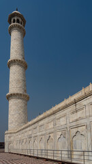 The high white marble minaret of the famous ancient Taj Mahal against the blue sky. A tower with...