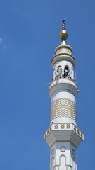 Fototapeta na wymiar Low angle view Single Minaret of Muslim mosque on the clear blue sky background. Islam, religion and architecture, and travel concept. Mosque design in Islamic religious architectural traditions.
