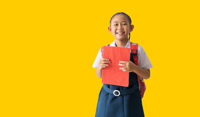 Happy Asian student child girl wears school uniform holding book, back to school, isolated on yellow background