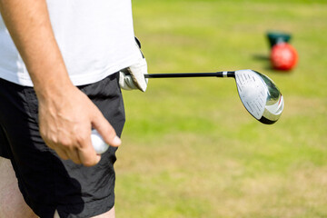 Hand of a golfer holding a golf ball, positioned sideways on a blurred background of a golf course.