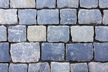 Old dark gray cobblestone pavement road from smooth stones as background top view close up