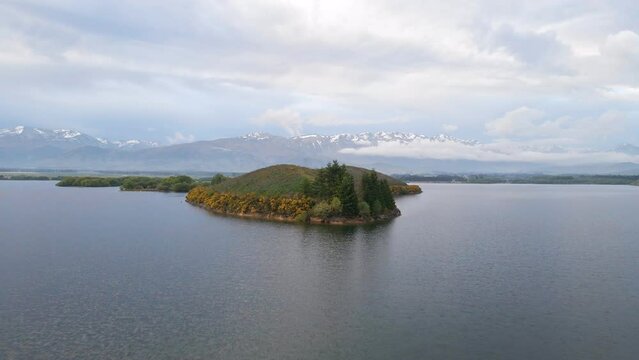 Drone flight over lush island on a lake and southern alps of New Zealand in background
