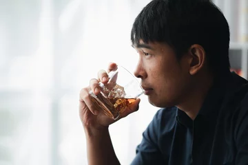 Foto op Plexiglas Man holding a glass of brandy, he is drinking brandy in a bar, drinking alcohol impairs driving ability and can damage health. The concept of drinking alcohol. © kamiphotos