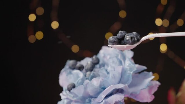 Blueberries falling onto white spoon and bouncing off blue flower