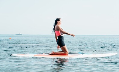 Woman sup yoga. Happy young sporty woman practising yoga pilates on paddle sup surfboard. Female stretching doing workout on sea water. Modern individual female outdoor summer sport activity.