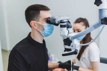 Modern dental office with a microscope. A dentist treats a man's teeth under a microscope, an assistant helps him. Modern medical care for toothache